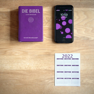 auf einem Tisch liegen eine Bibel, ein Handy und ein Kalender